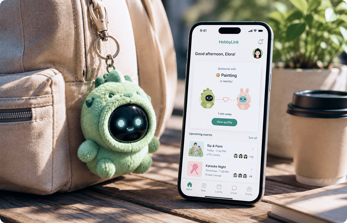 A green plush dinosaur mascot charm with a digital eyes screen clipped to a backpack, beside a phone showing the HobbyLink app notifying that someone with a shared interest in painting is nearby